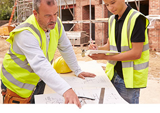 Two construction workers on a construction site looking at architectural drawings
